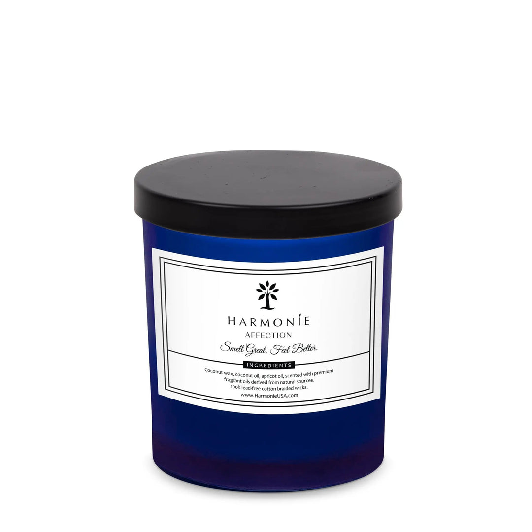 A blue glass jar of Harmonie brand candle with the label 'It Smells Like Affection Gardenia & Oud Wood'. The candle has a black lid.