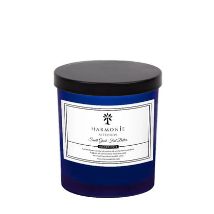 A blue glass jar of Harmonie brand candle with the label 'It Smells Like Affection Gardenia & Oud Wood'. The candle has a black lid.