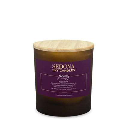 A Sedona Sky candle with a purple label, peony written in white, contained in a clear jar with a wooden lid, with a height ratio of approximately 2:1.