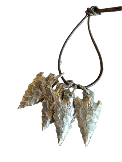 A silver handcrafted arrow head with a rope attached, displayed against a white background.