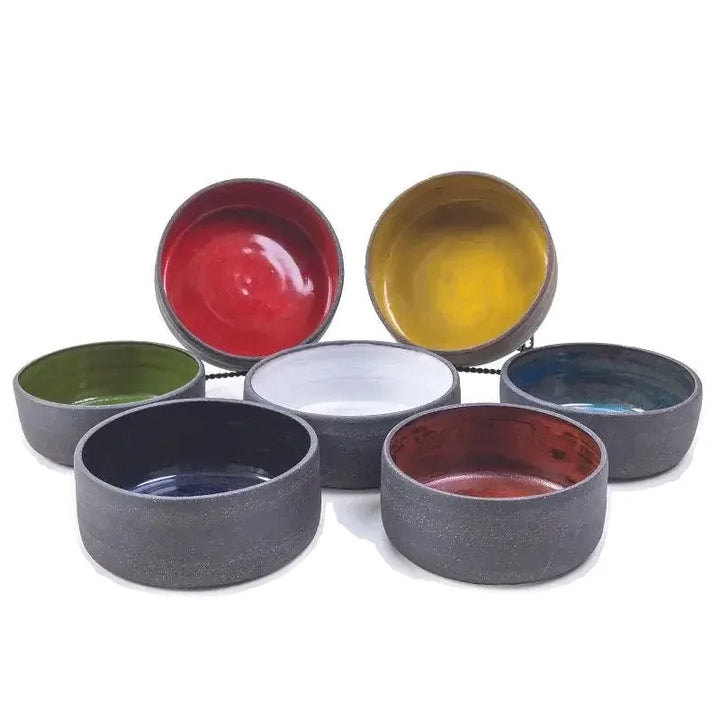 Six handmade ceramic vessels in red, yellow, blue, green, white, and grey glazes viewed from above