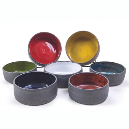 Six handmade ceramic vessels in red, yellow, blue, green, white, and grey glazes viewed from above