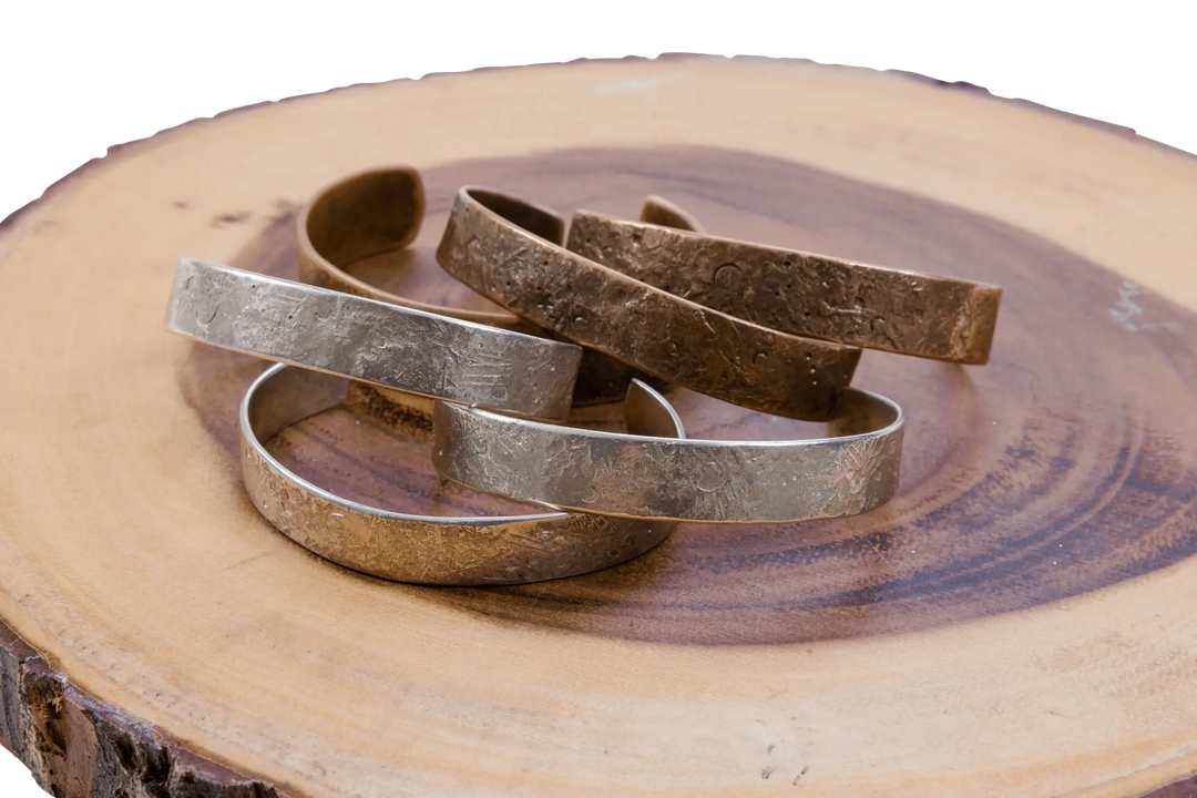 Hammered silver and copper cuff bracelets stacked on a live-edge wood slab