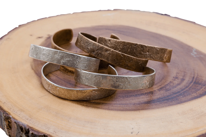 Hammered silver and copper cuff bracelets stacked on a live-edge wood slab