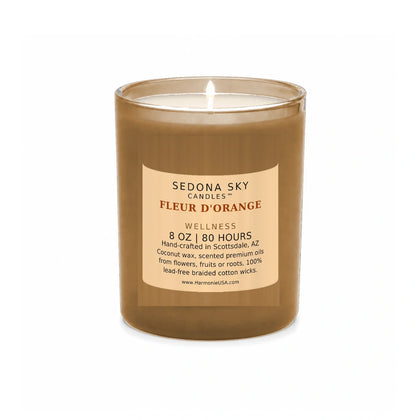 Sedona Sky Fleur d'Orange candle, 8 oz frosted coral glass jar with matte apricot label, lit wick and visible wax pool, on a seamless white background
