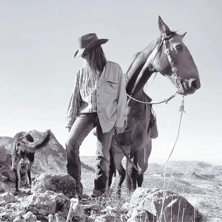 Archival black-and-white photograph of a ranch hand leading a saddled horse across West Texas rock