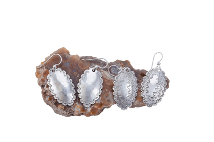 Two pairs of hammered Roosevelt dime earrings resting on a piece of raw agate